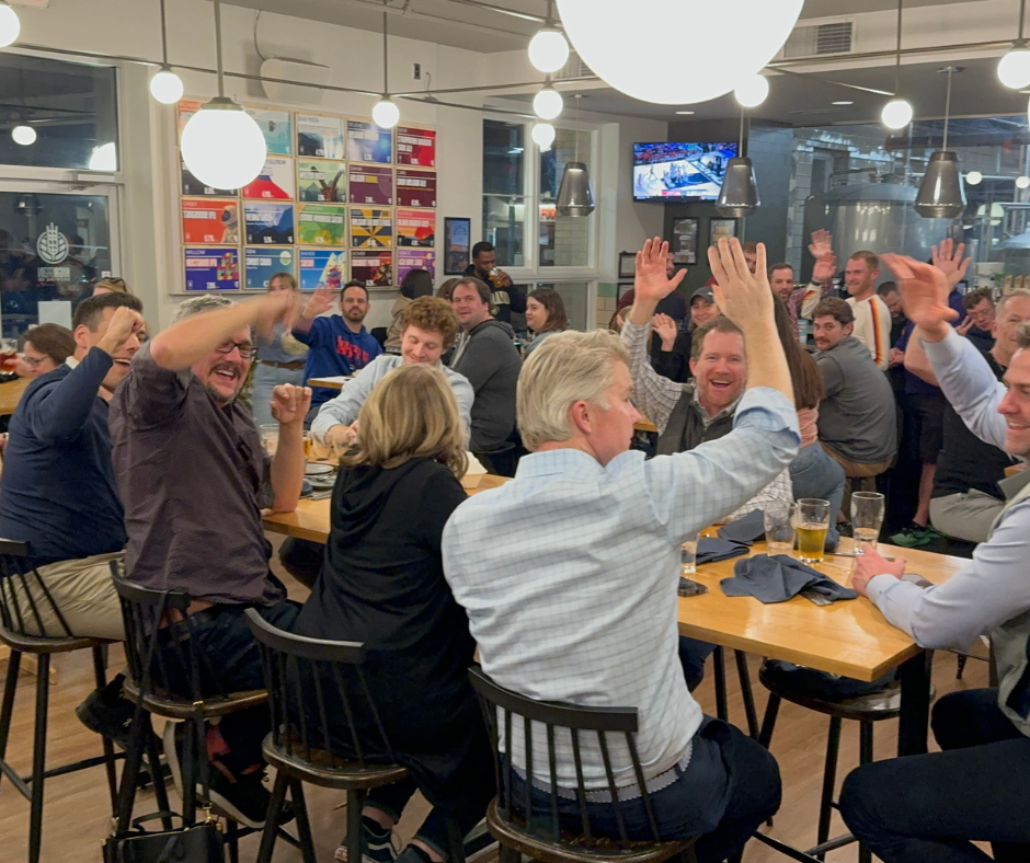 Don’t Make These 10 Trivia Night Mistakes at Your Bar 1 Large group of trivia players raising hands and cheering inside a busy brewery taproom