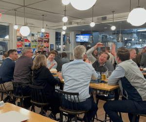 Group of adults celebrating and high-fiving at a brewery table during trivia night