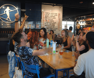 Group of friends cheering and celebrating a trivia win at a bar with drinks and laughter
