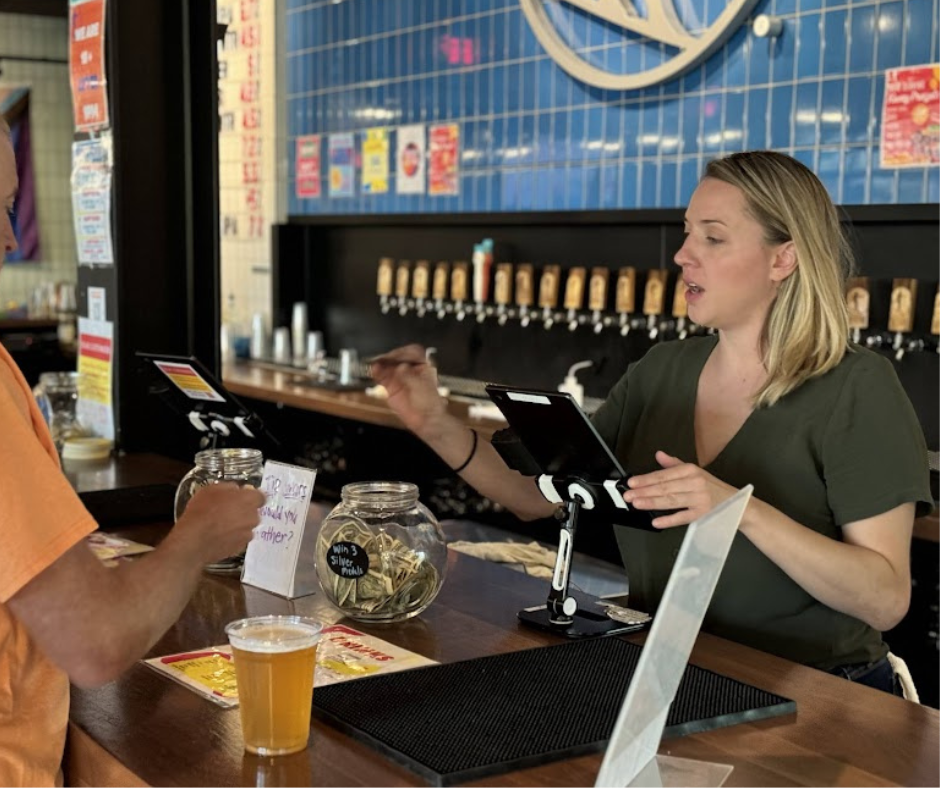 Don’t Make These 10 Trivia Night Mistakes at Your Bar 2 Bartender talking with a guest at a bar counter during a trivia night vote with tip jars and a tablet